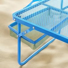 a blue metal table with two baskets on it's sides and sand in the background