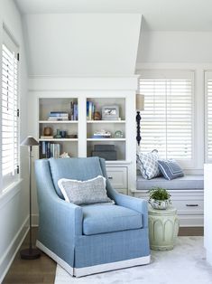 a blue chair sitting in front of a window next to a book shelf filled with books