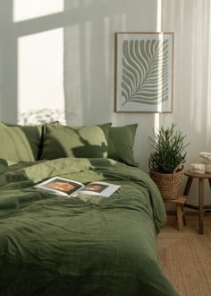 a bed with green sheets and pillows next to a potted plant on the floor