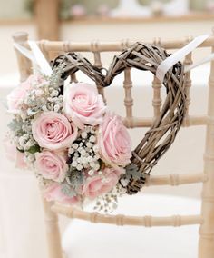 a heart shaped wreath with pink roses and baby's breath sits on a chair