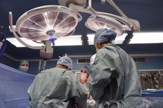 two surgeons performing surgery in an operating room with lights on and equipment hanging from the ceiling