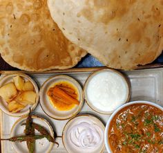 an assortment of food items on a tray with sauces and bread in the background