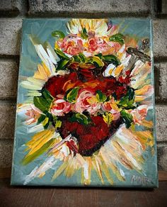 a painting with flowers in the shape of a heart on a wooden table next to a brick wall