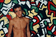 a shirtless man standing in front of a colorful wall