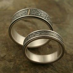 two wedding rings sitting on top of a stone slab with engraved designs in the middle