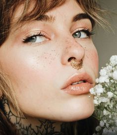 a close up of a woman with flowers in her mouth and nose piercings on