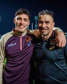 two men standing next to each other in front of a soccer field with the lights on