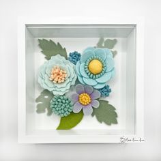 paper flowers in a white frame with green leaves