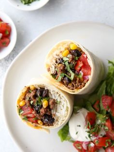 two burritos on a plate with salsa and lettuce next to it