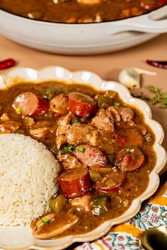 a white plate topped with rice and meat next to a bowl of soup on a table