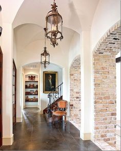 a hallway with a chandelier hanging from the ceiling next to a brick wall