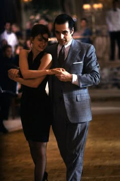 a man in a suit and tie dancing with his arm around a woman's waist