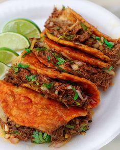 some tacos are on a white plate with lime wedges and cilantro