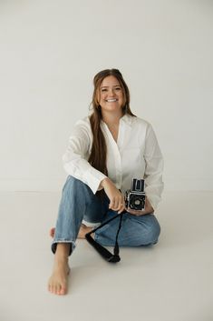 a woman sitting on the floor with a camera in her hand and smiling at the camera