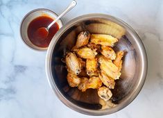 a metal bowl filled with fried bananas next to a cup of ketchup on a marble table