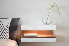 a white nightstand with a flower in a glass vase on it next to a bed