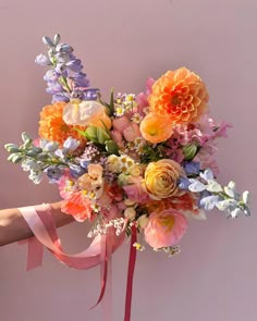 a bouquet of flowers is being held by a woman's hand with a pink ribbon