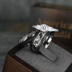 two wedding rings sitting on top of each other in front of a wooden box with an engraved band