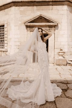 a woman in a wedding dress with a veil on her head standing next to a building