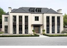 a large white house with black windows and bushes in front of the entrance to it