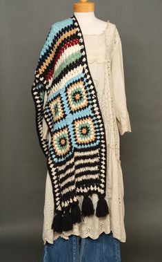 a crocheted shawl with tassels and fringe on it, sitting on top of a mannequin