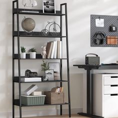 a black book shelf sitting on top of a wooden floor next to a white desk