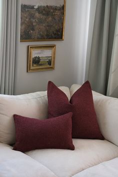 two red and white pillows sitting on top of a white couch next to a window