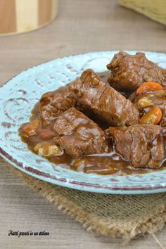 a blue plate topped with beef and carrots covered in gravy on top of a wooden table