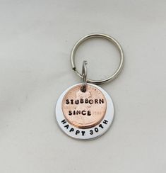 a silver and copper keychain with the words stubborn since happy sorry on it