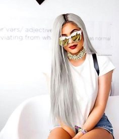 a woman with long grey hair and sunglasses sitting on a white couch wearing fishnet stockings