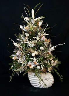 a white vase filled with lots of different types of flowers and plants on top of a black background