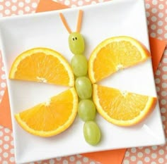 a plate with oranges, grapes and an insect made out of fruit on it