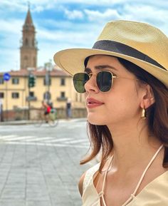 a woman wearing sunglasses and a hat standing in front of a building with a clock tower