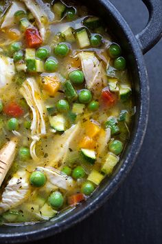 a pot filled with chicken and vegetables on top of a table next to a wooden spoon