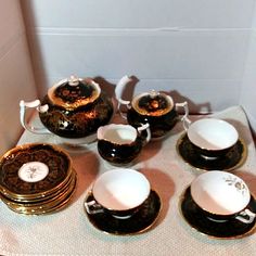 a table topped with black and gold tea set on top of a cloth covered table