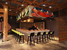 a restaurant with wooden tables and yellow bar stools in front of a mural hanging from the ceiling