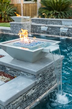 an outdoor fire pit in the middle of a pool with water running from it's sides