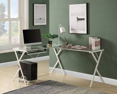 a computer desk with a laptop on top of it in front of a green wall