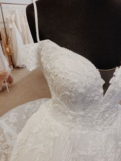 the back of a wedding dress on display at a bridal fashion store, with mannequins in the background