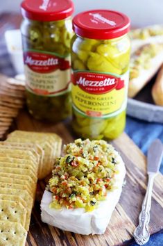 two jars of pickles and crackers sit on a cutting board next to bread