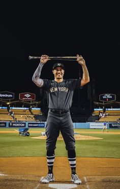 a man holding a baseball bat over his head on a baseball field in front of an empty stadium