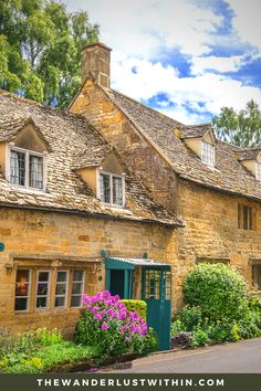 an old stone house with green shutters and flowers in the front yard on a sunny day