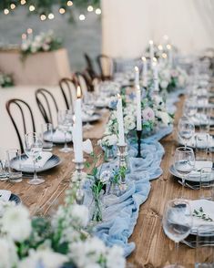 a long table is set with white and blue flowers, candles, and napkins