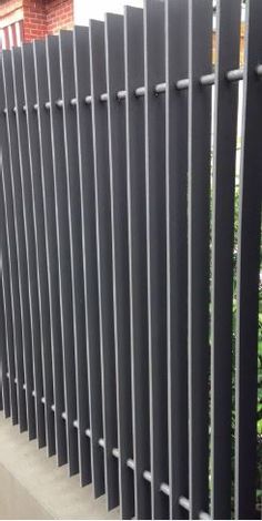 a black metal fence next to a brick wall and shrubbery in front of it