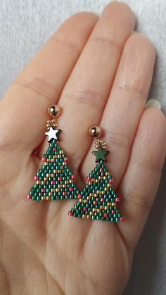 a pair of green and red beaded christmas tree earrings on a person's hand