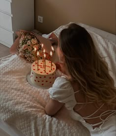 a woman laying in bed next to a cake with lit candles on top of it