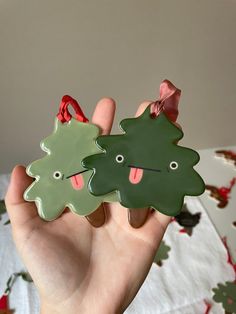 a hand holding two christmas ornaments in the shape of trees