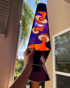 a hand is holding up a stained glass vase in front of a window with palm trees