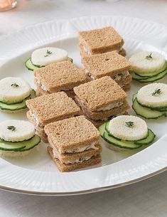 small sandwiches are arranged on a plate with cucumber slices and herbs in the middle