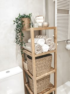 a wooden shelf with baskets and towels on it next to a toilet in a bathroom